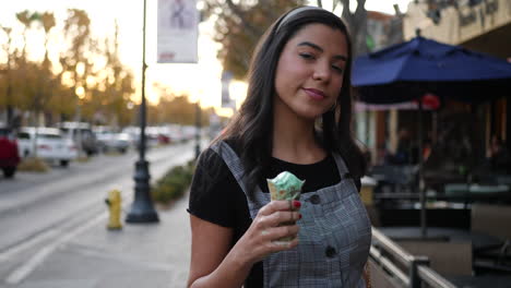 adult hispanic woman eating a messy, dripping ice cream cone dessert on the city street at sunset slow motion