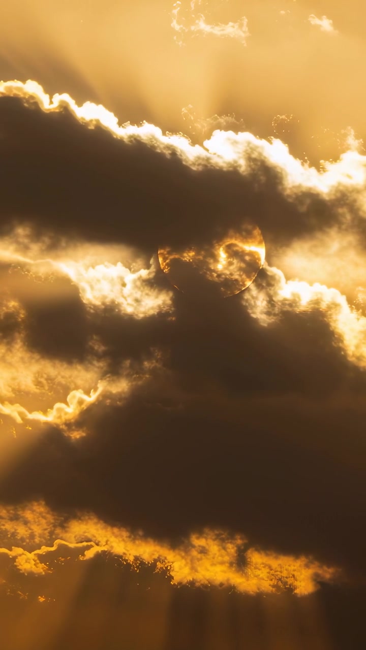 Vertikales Video: Sich verschiebende, zentral von hinten beleuchtete Wolkenbank enthüllt die Sonne und wirft Sonnenstrahlen von der tiefstehenden Sonne.