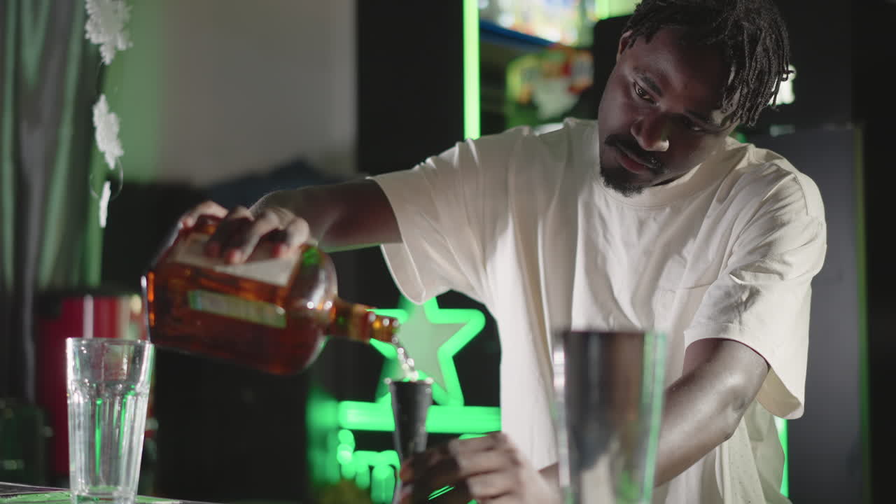 Bartender pouring whiskey from bottle into glass on bar counter in modern bar with green neon lighting, focused on drink creation, professional bartending skills