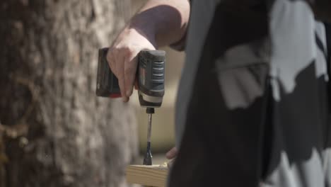 a man uses a drill to drill hole into board