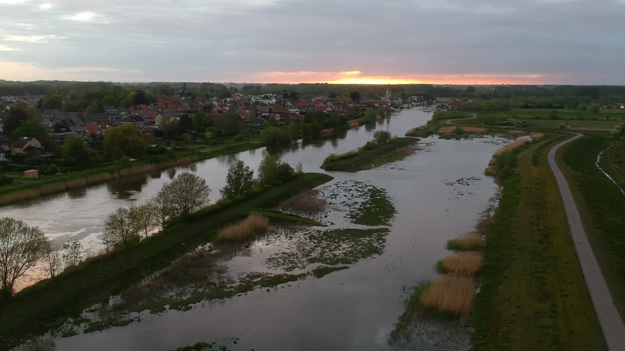 Panoramaudsigt fra luften over sump og huse i baggrunden ved solnedgang.