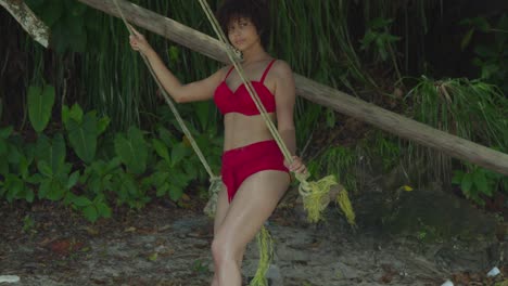 on a sunny day, a tropical island becomes the setting for a young girl in a red bikini with curly hair on a swing