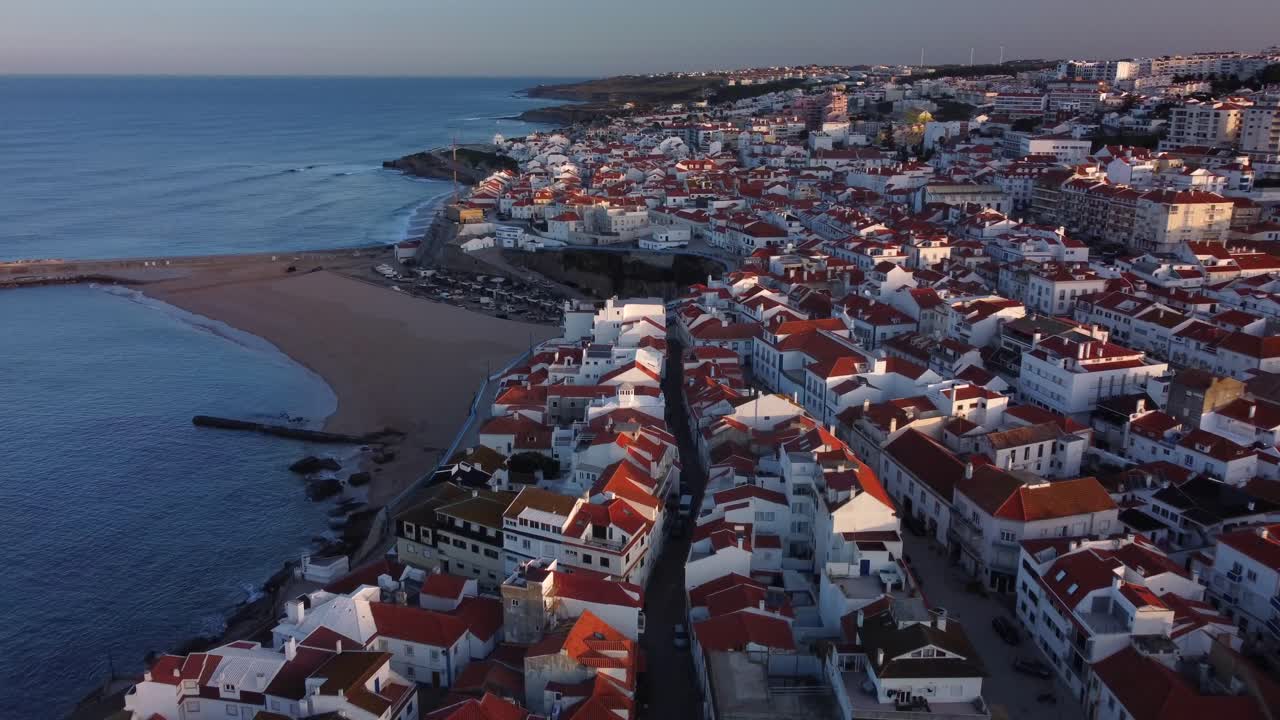 Allontanamento aereo dalle case costiere di Ericeira che rivela una splendida città del surf al mattino, Portogallo.