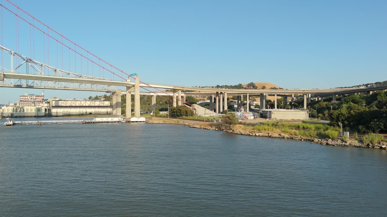 Right to left aerial pan highlights the industrial textures of Crockett contrast with the modern engineering of the Alfred Zampa Bridge, captured during a soft afternoon light