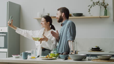 pareja alegre haciendo una foto selfie con ensalada en una cocina moderna