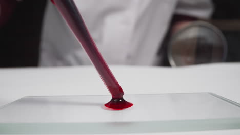 specialist in robe drips blood onto slide in laboratory