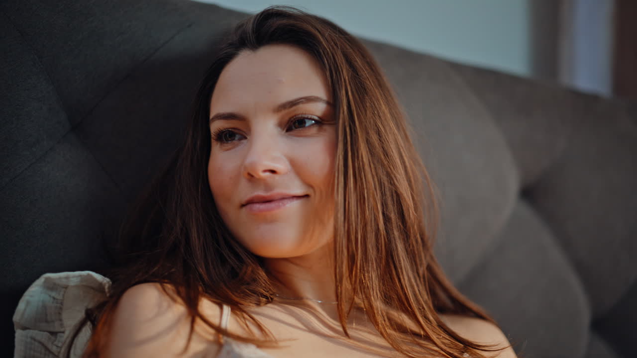 Smiling woman reading cellphone message lying modern bedroom interior closeup