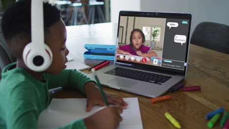schoolboy using laptop for online lesson at home, with schoolgirl and web chat on screen