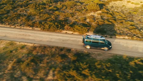 Viejo-Y-Nostálgico-Autobús-Furgoneta-Con-Tablas-De-Surf-En-El-Techo-Conduce-A-Lo-Largo-De-Una-Carretera-Polvorienta-En-Un-Paisaje-Mediterráneo