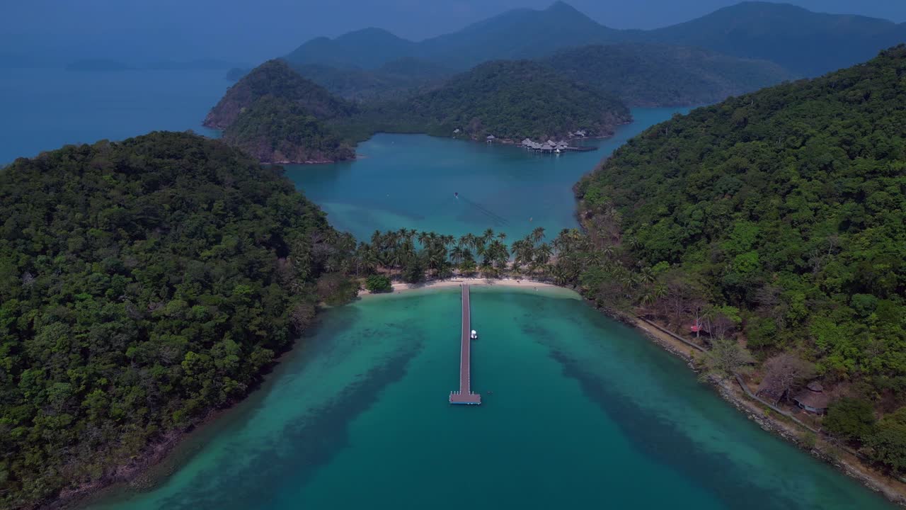 Koh Chang's idyllic landscape, featuring lush greenery, a pristine beach, and a tranquil pier extending into the turquoise waters. Majestic aerial view flight drone shot footage from above