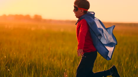 un niño con un disfraz de superhéroe al atardecer corre por el campo riendo y sonriendo.