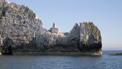 rocky sea stacks with seabirds perched atop, under a clear blue sky, surrounded by calm ocean waters