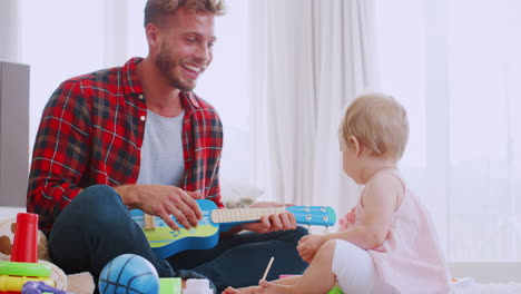 Young-dad-playing-ukulele-with-toddler-daughter,-close-up