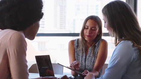 Un-Equipo-Empresarial-Multicultural-Femenino-Se-Reúne-Alrededor-De-Una-Mesa-De-Juntas-Con-Una-Computadora-Portátil-Y-Una-Tableta-Digital