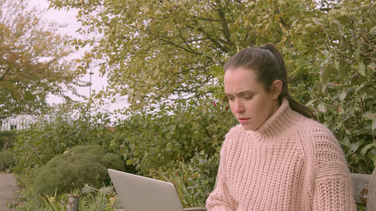 Female working on a laptop in a park determined