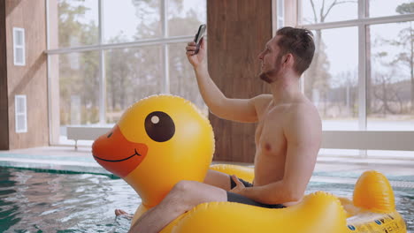 adult happy man is calling by video from modern water park sitting on funny inflatable circle swimming pool