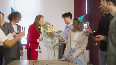 사무실에서 그녀의 다민족 동료들에 의해 surronded 케이크에 촛불을 끄는 행복한 여자 1