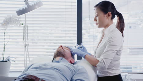esteticista dando a una paciente femenina madura una inyección de botox en la frente