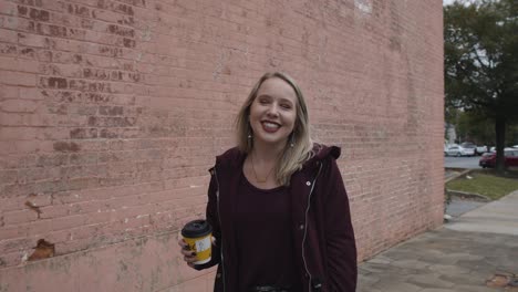 slow motion shot of a young female smiling and walking down the street with a coffee cup in hand