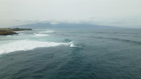 Aerial-view-on-group-of-surfers-riding-wave-at-Paia-Beach,-Maui,-Hawaii