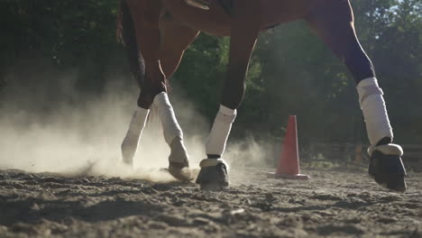 el caballo y la jinete femenina trotan hacia la cámara en una arena arenosa con pilones al lado