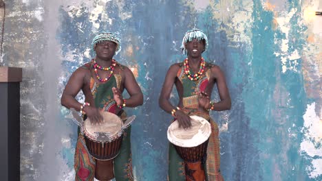 two african artists in colorful costumes playing djemba drums