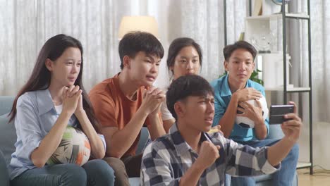 asian teenagers cheering and watching football game on smart phone and celebrating victory at home