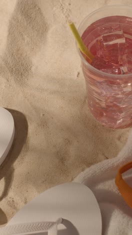 Vertical-Video-Summer-Holiday-Concept-Of-Flip-Flops-With-Cold-Drink-On-Sand-Background-With-Tree-Shade-Shadow