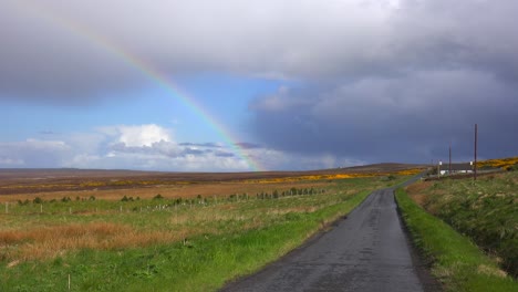 a beautiful rainbow forms along a one lane road in scotland or ireland