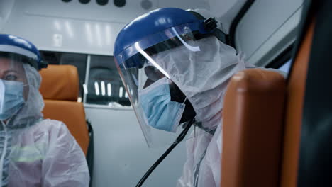 black paramedic riding ambulance with colleague low angle of tired african american male doctor in hazmat suit sitting near female colleague while riding ambulance during coronavirus pandemic