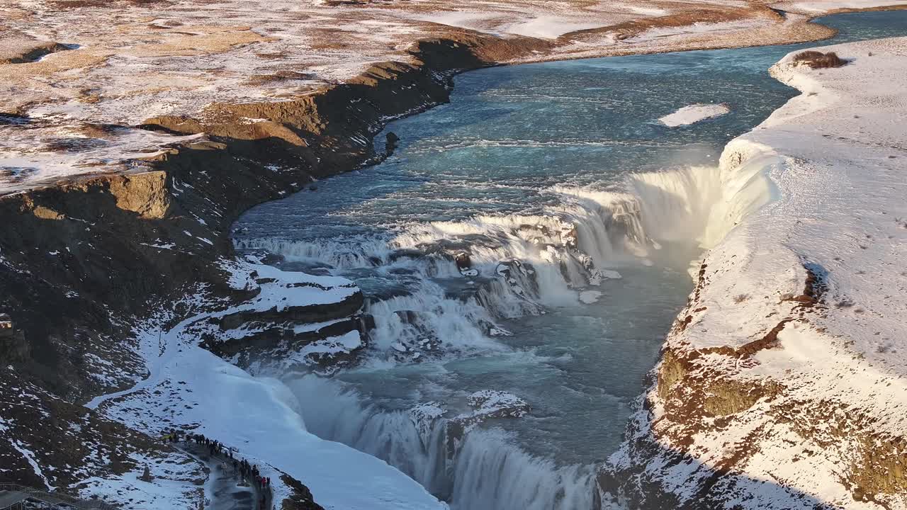 Aerial view looking down into Gullfoss waterfall, Iceland. Powerful turquoise water plunging into a snowy canyon.