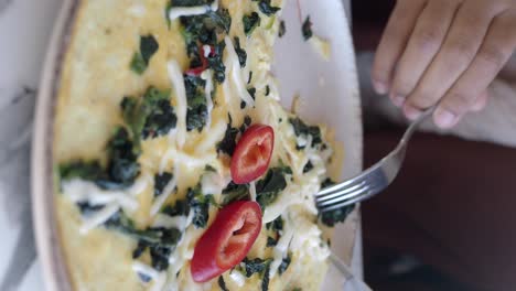 a person eating a delicious omelet with spinach, cheese and red pepper