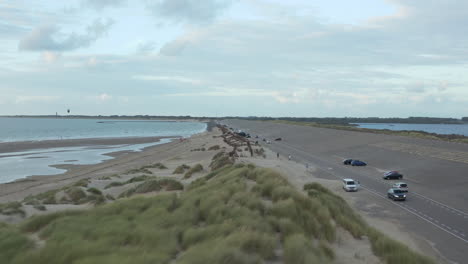 Niedriger-Flug-über-Dünengras,-Das-Im-Wind-Weht,-Und-Möwen,-Die-In-Der-Nähe-Des-Strandes-Mit-Bewölktem-Himmel-Vorbeiziehen