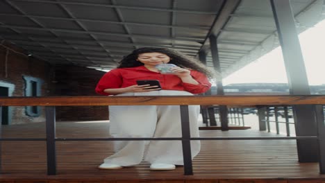 woman enjoying a drink and using her phone on a porch