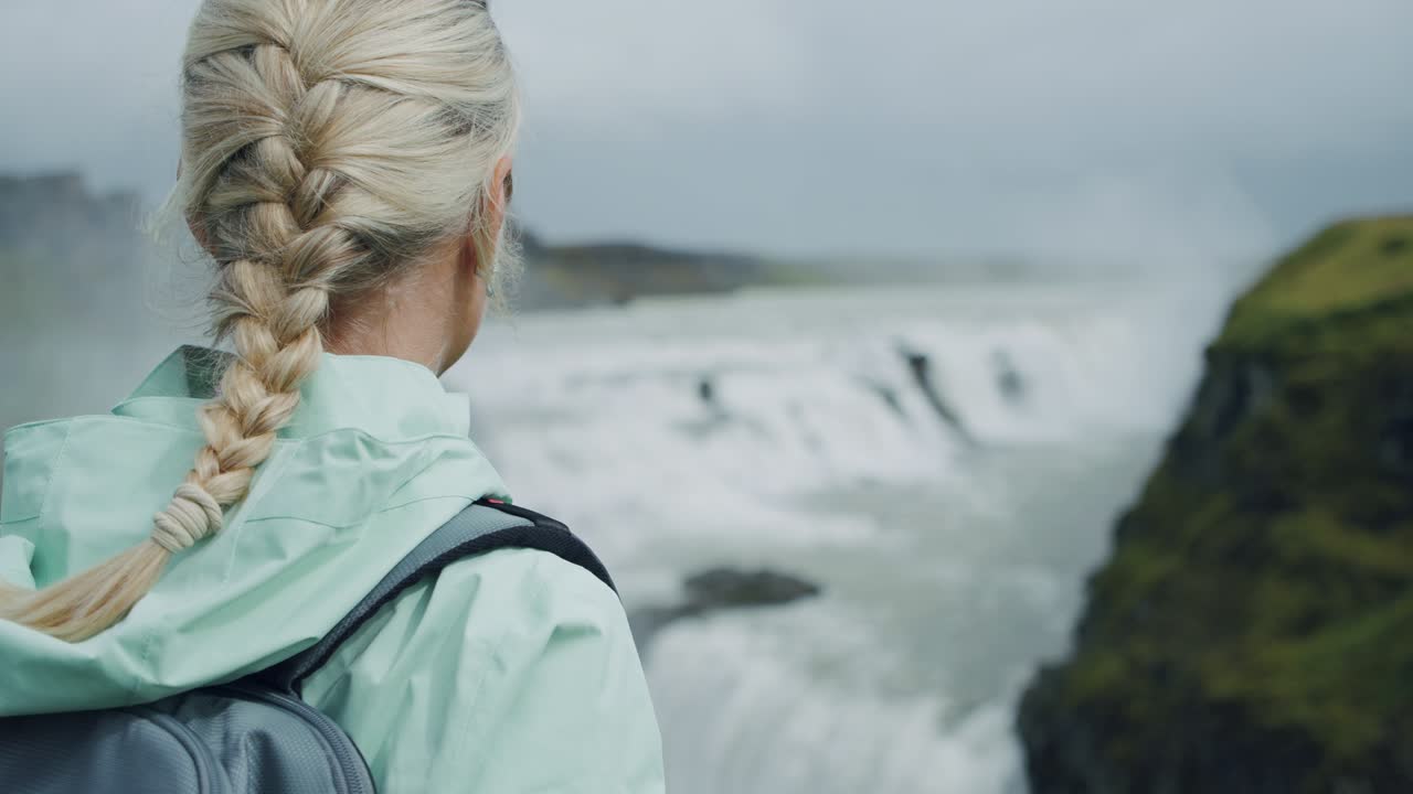 배을 들고 여행하는 여성이 gullfoss 폭포를 즐기는 뒷면. 아이슬란드의 유명한 관광 명소이자 랜드마크 목적지입니다.