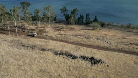 Aerial-drone-view,-backwards-movement:-flying-over-a-country-road-by-the-sea,-with-a-lone-car-going-somewhere