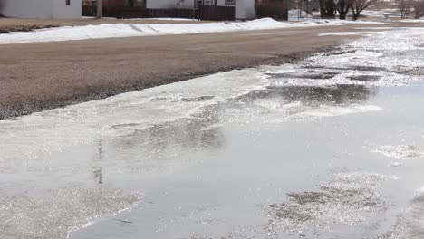 A-stream-of-water-flowing-down-hill-in-a-bank-of-ice-next-to-a-road