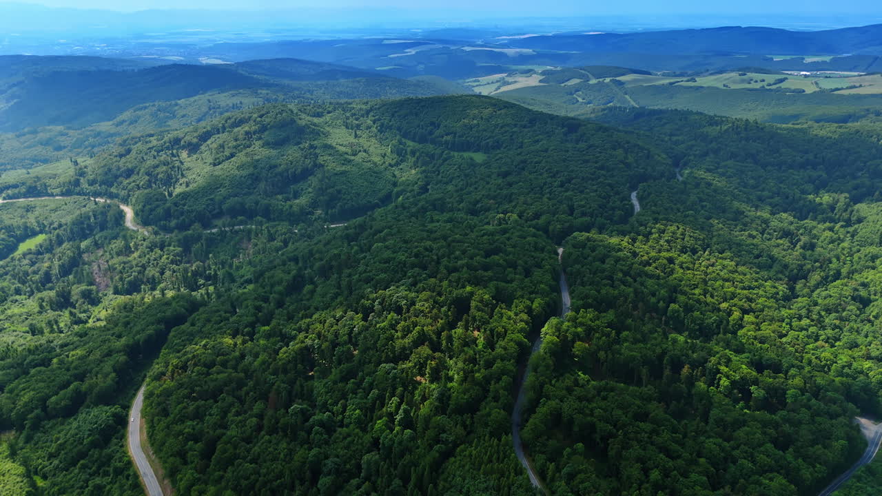 Expansive aerial view of forested mountain ranges.. Drone panorama of green mountains and valleys. The forest landscape extends to the horizon under a blue sky