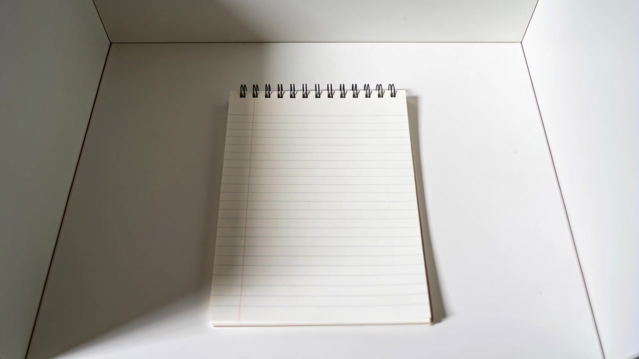 Zooming camera moving forward, framing spiral notepad in white lightbox for product catalog