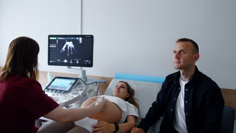 female doctor performs ultrasonic check for pregnant woman. expecting parents look attentively on the monitor.