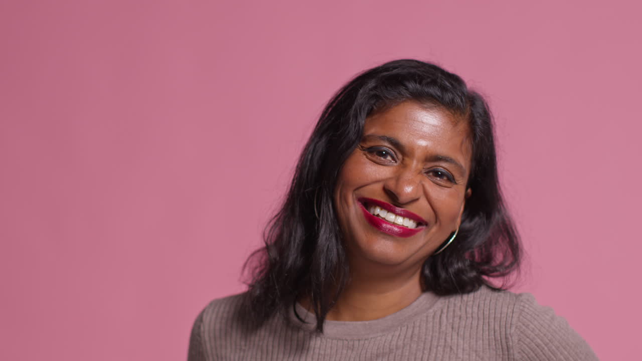 retrato de estudio de una mujer madura sonriente que lleva y señala una cinta rosa de concienciación sobre el cáncer de mama contra un fondo rosa