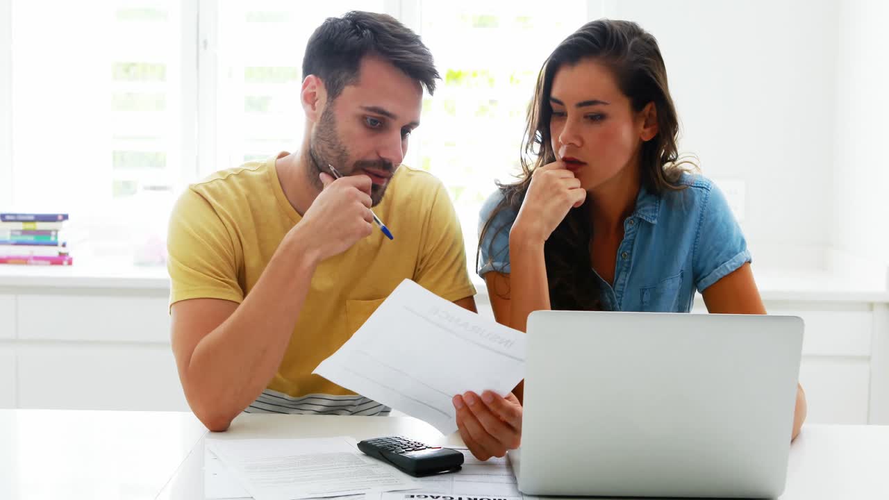 pareja preocupada calculando sus facturas con una computadora portátil en la cocina