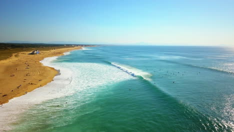 cinematic aerial drone follow backwards morning crowd of surfers huge waves glassy swell surf hossegor seignosse france yellow sunrise sunset on beach mountain sandy coast biarritz basque country