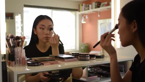 a young woman applying makeup at her vanity table, showcasing a variety of cosmetic products in a brightly lit room