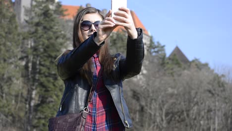 encantadora joven con cabello castaño haciendo fotos selfie en un parque público en una agradable tarde soleada