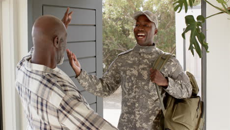 Welcoming home, man in military uniform hugging older man at doorway