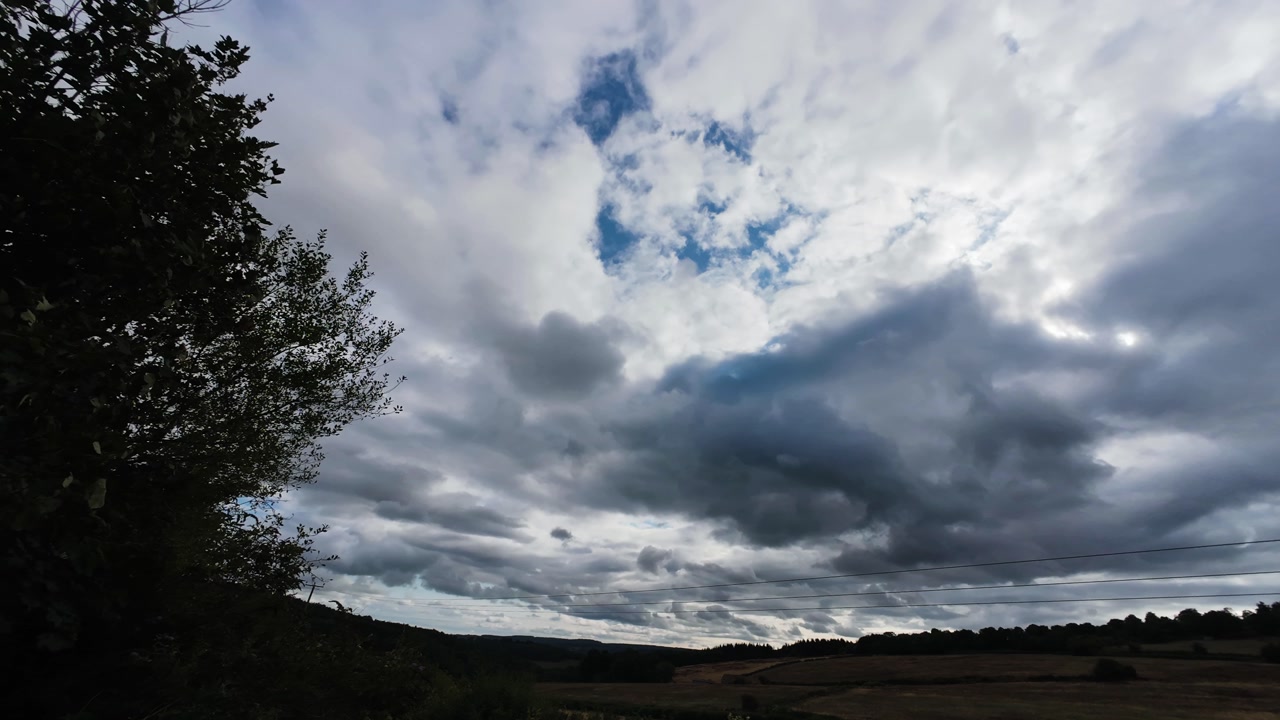 Fast Moving Timelapse of Clouds Moving Quickly Over the Sky with Silhouetted Trees in British Countryside.