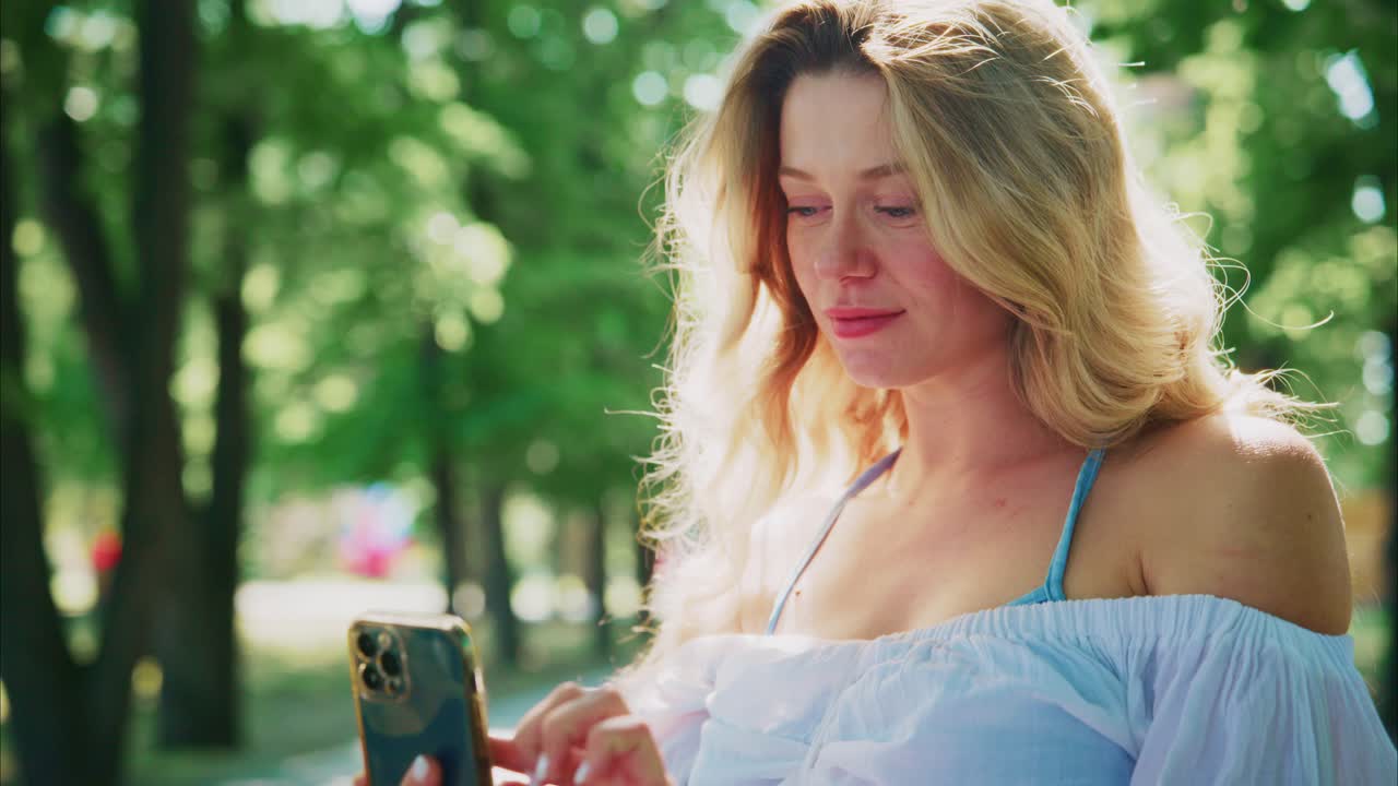 Junge Frau lächelt und benutzt Smartphone im sonnigen Park