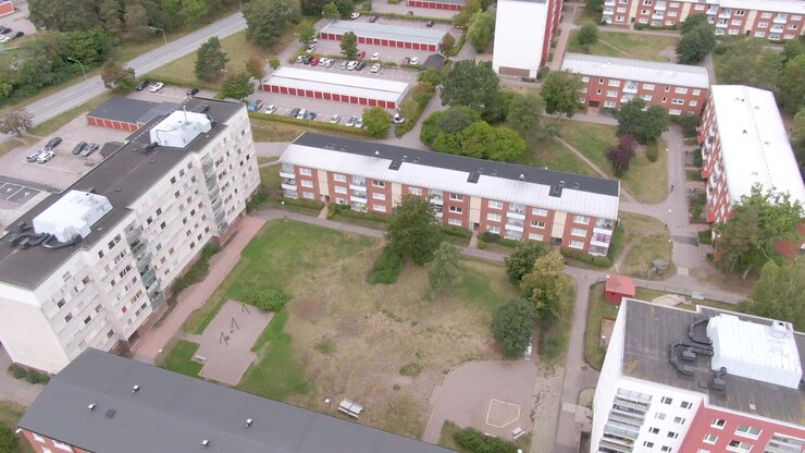 Veduta dall'alto di appartamenti attorno a un prato irregolare con sentieri, parco giochi, parcheggio e garage con tetto a capanna rosso