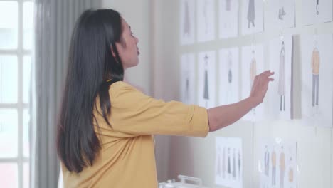 vista lateral de una diseñadora con una máquina de coser mira las imágenes en la pared y piensa mientras diseña ropa en el estudio